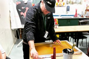 A person in a black top and cap does screen printing
