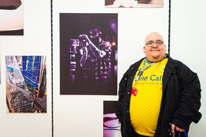 A volunteer in a yellow shirt stands with the photograph wall